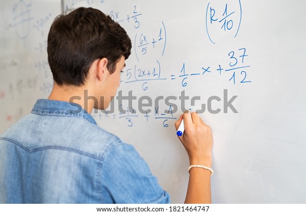 Back view of high school student solving math\
problem on whiteboard in classroom. Young man writing math solution\
on white board using marker. College guy solving math expression\
during lesson.