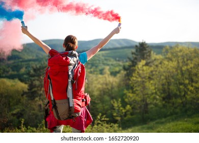 Back View Of Hiker Girl With Backpack While Sends Red And Blue Smoke Signal