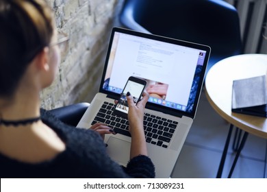 Back view of hipster girl reading advertise news on mobile phone version of website. Female watching training webinar on computer. Woman making synchronization of files with laptop application - Shutterstock ID 713089231