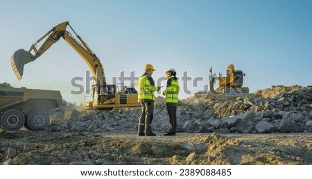 Back View Of Hispanic Female Project Manager And Caucasian Male Civil Engineer Discussing New Real Estate Project On Construction Site. Industrial Excavators Digging The Ground For Building Foundation