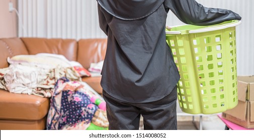 Back View Of Housewife Holding Green Empty Basket To Clean The Messy Living Room.