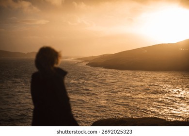 A back view of human standing and looking to sea during sunset
