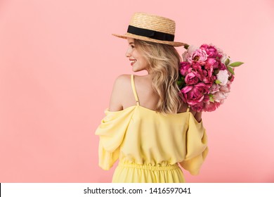 Back view image of a beautiful amazing young blonde woman posing isolated over pink wall background holding flowers.