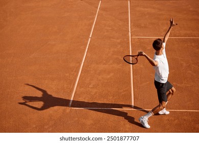 Back view image of focused young man in white t-shirt and black shorts, tennis player training on clay court. serving ball with racket. Concept of sport, competition, active and healthy lifestyle - Powered by Shutterstock