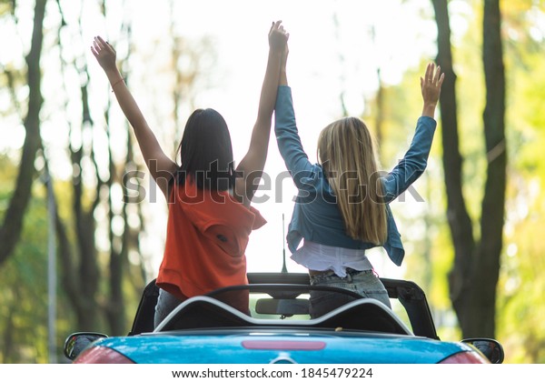 Back view image of a gorgeous\
pretty young of two women friends driving the car with raised\
hands.