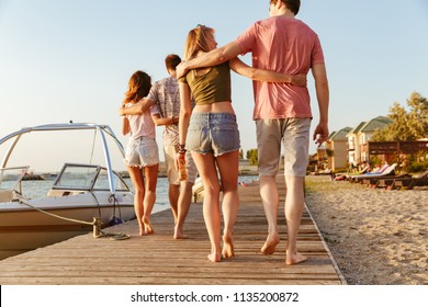 Back view image of group of four friends loving couples walking outdoors on the beach.