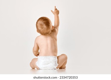 Back view image of little baby, child, toddler sitting in diaper against white studio background. Curious baby. Concept of childhood, newborn lifestyle, happiness, care. Copy space for ad - Powered by Shutterstock