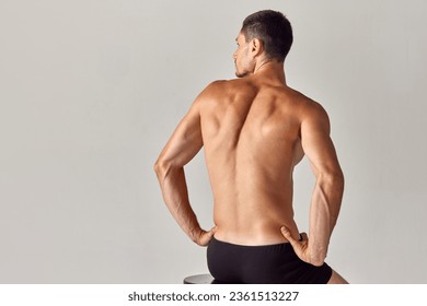 Back view image of muscular young shirtless man with relief, sign back sitting in underwear against grey studio background. Concept of men's health and beauty, body care, fitness, wellness, ad - Powered by Shutterstock