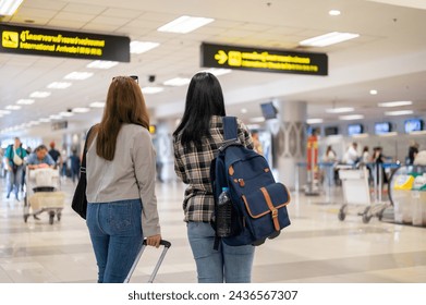 A back view image of two Asian female friends, travelers, walking in the airport, looking for their check-in counter. people and transportation concepts