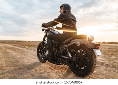 Back view image of young man biker on bike outdoors at the desert field in helmet.