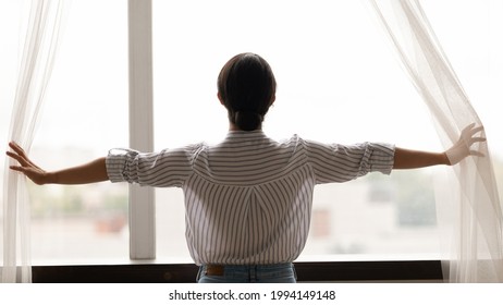 Back View Of Indian Woman Open Curtains Meet Welcome New Sunny Day In Cozy Home. Mixed Race Ethnicity Female Renter Enjoy Window View, Excited About Life Perspective Or Opportunities. Vision Concept.