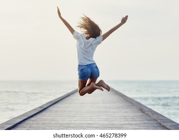 Back View Of Jumping Girl On The Pier. Freedom Concept 