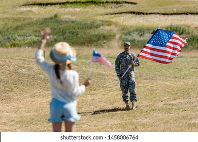 Back View Of Kid In Straw Hat Waving Hand While Holding American Flag Near Man In Military Uniform 