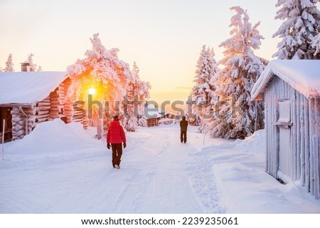 Back view of kids walking among wooden huts and snow covered trees in Lapland Finland