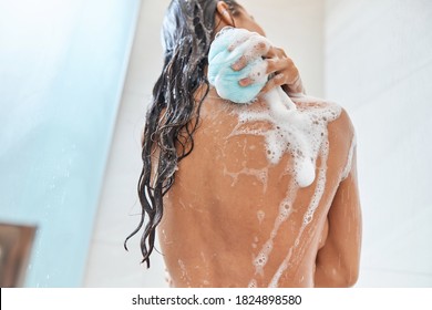 Back View Of Lady With Foam On Her Skin Using Blue Bath Loofah While Taking Shower At Home