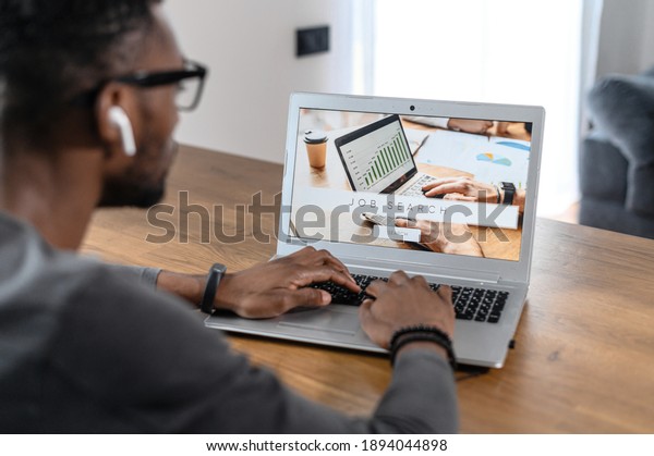 Back view\
laptop screen with a page with job search site on it, an African\
male millenial looking for new vacantions, position, jobless man is\
using app for fast job\
searching
