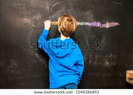 Back view of a little boy painting something on a chalkboard.