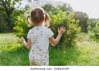 Back view little caucasian happy kid girl 5-6 years old in white casual clothes blow bubbles play on park green sunshine lawn, spending time outdoor in village countyside during summer time vacations - Shutterstock ID 2140615199