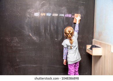 Back view of a little girl cleaning chalkboard.