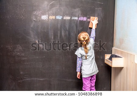 Back view of a little girl cleaning chalkboard.