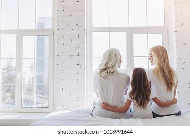 Back view of little girl, her attractive mother and charming grandmother are sitting on bed while spending time together at home. Women's generation. International Women's Day. Happy Mother's Day. - Powered by Shutterstock