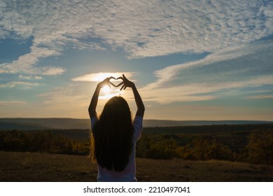 Back View Of Little Girl Making Heart Sign At Summer Sunset.