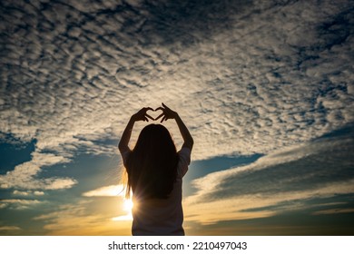 Back View Of Little Girl Making Heart Sign At Summer Sunset.