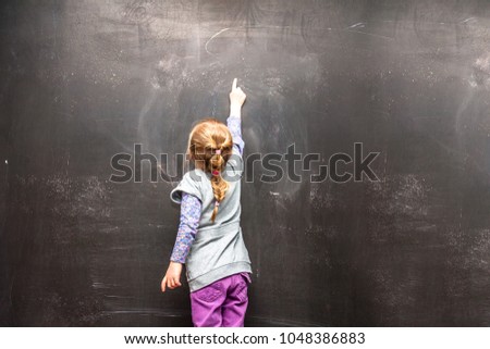 back view of a little girl ponting to something on a chalkboard.