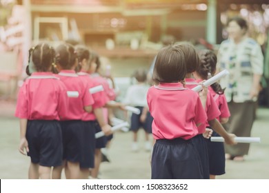 Back View Of Little Girls Use Paper Rolls Instead Of Long Cheerleader Baton Sticks For School Parade Marching Practice.