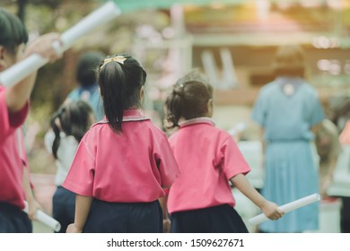 Back View Of Little Girls Use Paper Rolls Instead Of Long Cheerleader Baton Sticks For School Parade Marching Practice.