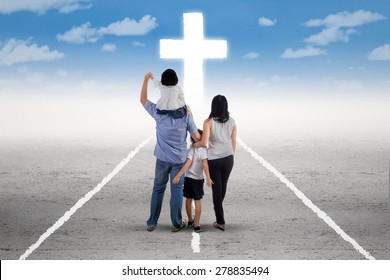 Back view of little happy family standing on the road and follow a cross