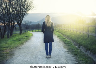 Back View Of Lonely Blonde Woman Standing On The Sunny Path In The Park.