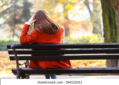 Back view of lonely young brunette woman sitting on a bench in the park