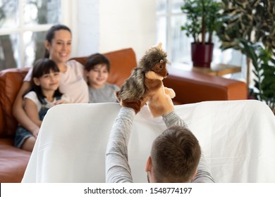 Back View Of Loving Dad Play With Toys Showing Puppet Show To Excited Little Preschooler Boy And Girl Kids, Happy Small Children Sit On Couch With Mom Enjoy Family Time Relaxing With Parents At Home