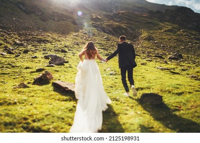 Back view of loving newlyweds, bride in wedding dress running to the top of the mountain. For lifestyle design.