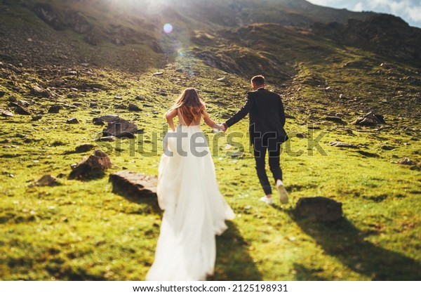 Back view of\
loving newlyweds, bride in wedding dress running to the top of the\
mountain. For lifestyle\
design.