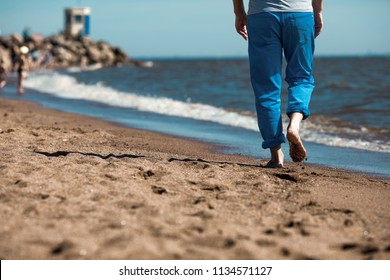 Back view of low section of barefoot man moving along coastline on wet sand