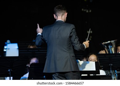 Back View Of A Male Band Conductor In Formal Suit Conducting His Concert Band