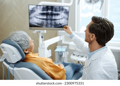 Back view of male dentist pointing at tooth X-ray image on screen during consultation in modern dental clinic - Powered by Shutterstock