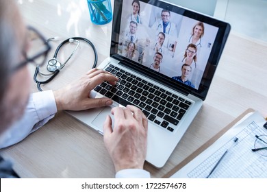 Back View Of Male Doctor Having Video Conference On Laptop With His Colleagues At Home.