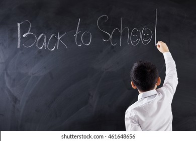 Back view of male elementary school student writes text Back to School on the Blackboard, shot in the class