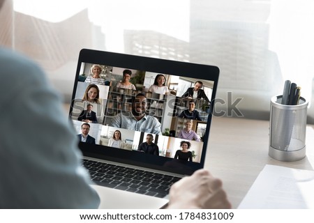 Back view of male employee have online video call on laptop with diverse multiethnic colleagues, man worker involved in webcam conference or virtual event on computer with multiracial businesspeople