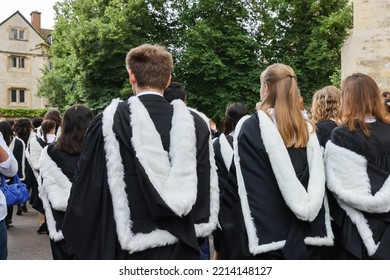 Back View Of Male And Female Fresh Graduate Students With Gown And Academic Address Walk In Cambridge University Campus, UK During Congregation Day.