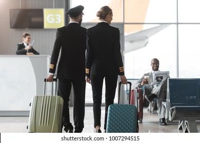 back view of male and female pilots walking by airport lobby with suitcases