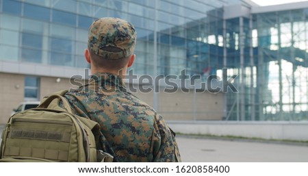 Back view of male soldier leaving on military service. Man in military uniform putting bag on shoulder and walking to airport terminal. Concept of military service, army, duty
