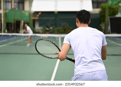 Back view of male tennis player focused in ready position to receive a serve, practicing for competition on a court - Powered by Shutterstock