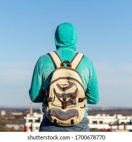 Back view of a man with a backpack on his back, standing on the roof of a house and looking at the city. Roof walking concept.