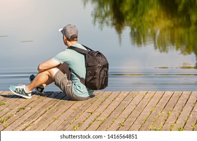 Back View Of Man With Backpack Sitting On A Pier