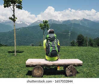 Back view of man with backpack sitting on wooden bench at mountains background in Krasnaya Polyana resort, Sochi, Russia