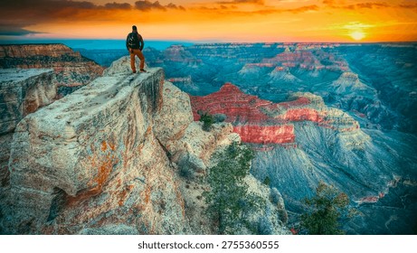 Back view of a man with backpack standing on a cliff edge overlooking the vast Grand Canyon National Park during a golden sunset, USA